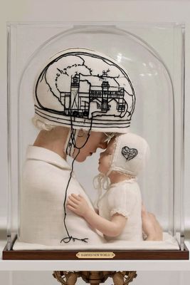 Bestickte Figuren von Mutter und Kind unter einer Glasglocke